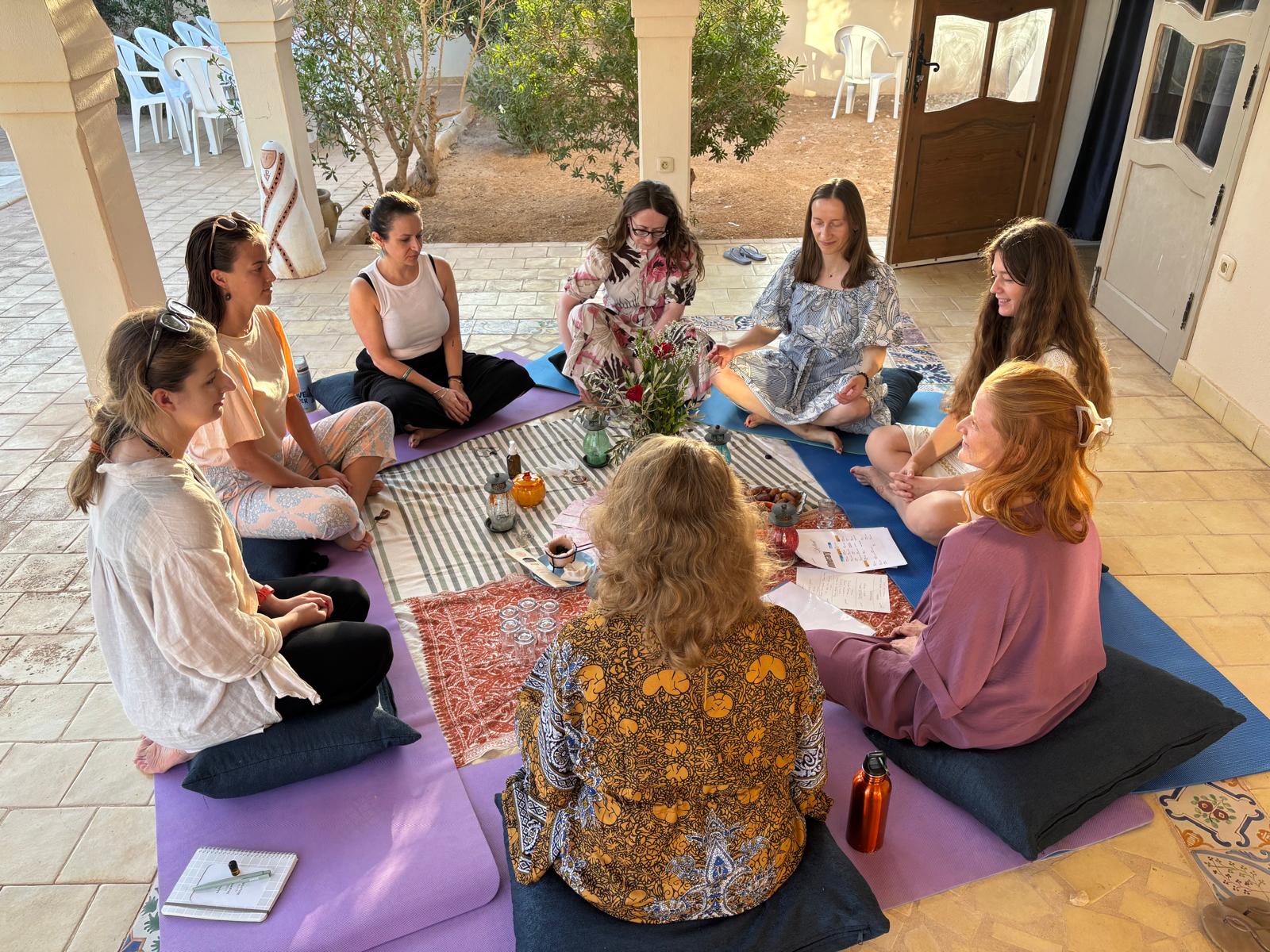Sharing circle seated on mats around flowers and candles